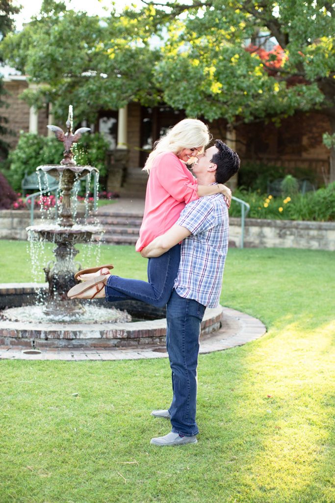 Guy lifting girl up kissing her next to fountain at Gilcrease Museum engagement