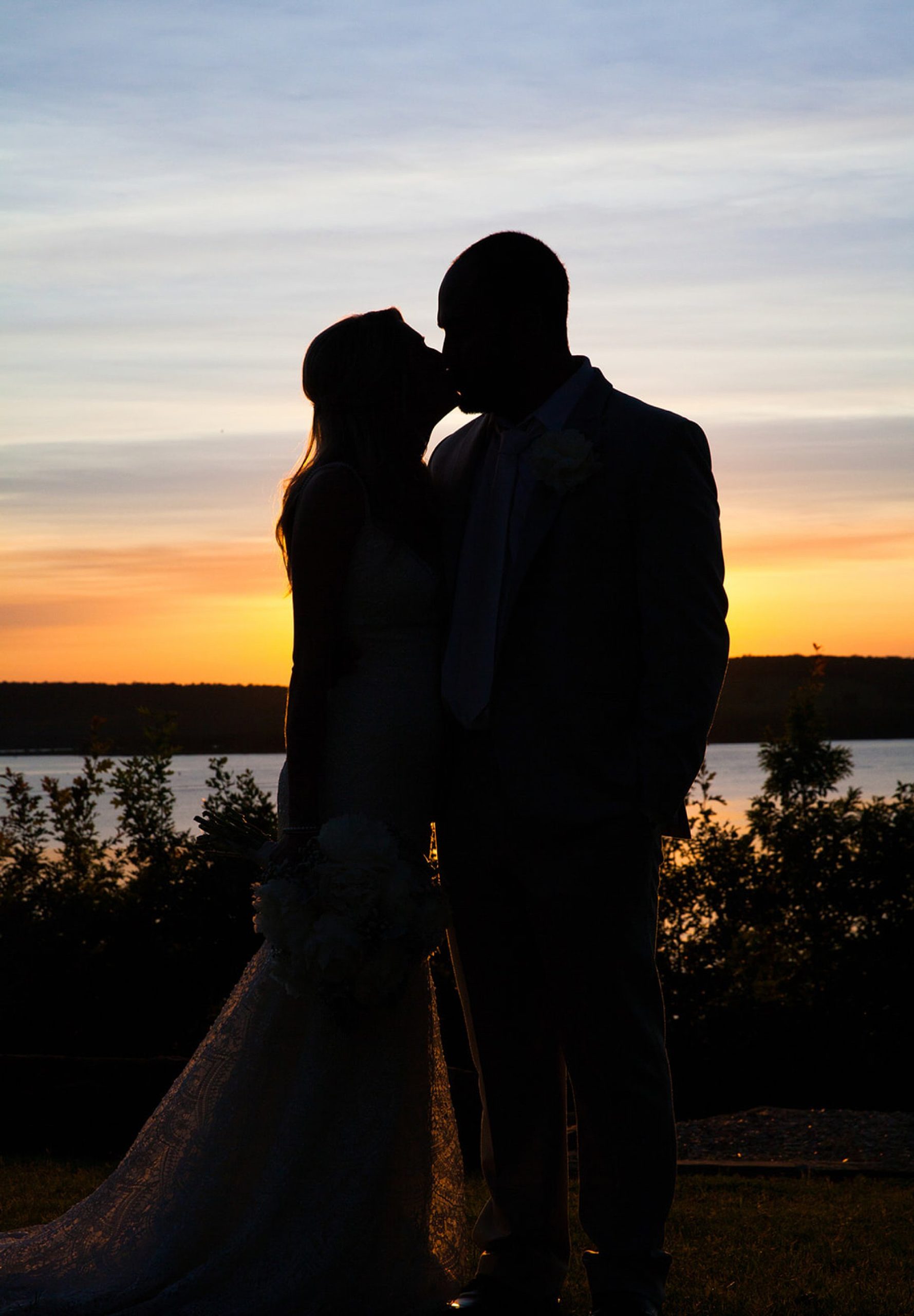 Silhouette of bride and groom kissing in front of lake at sunset at The Springs wedding event center