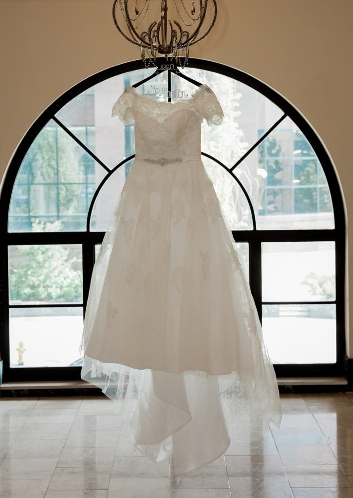 Wedding dress hanging from chandelier in front of window